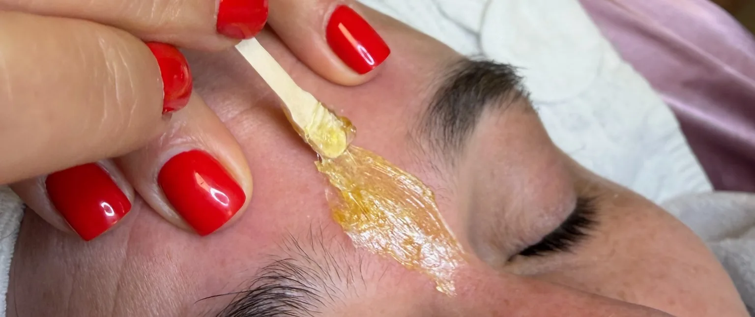 Wax szőrtelenítés az arcon: meleg wax felvitele spatulával a szemöldök környékén